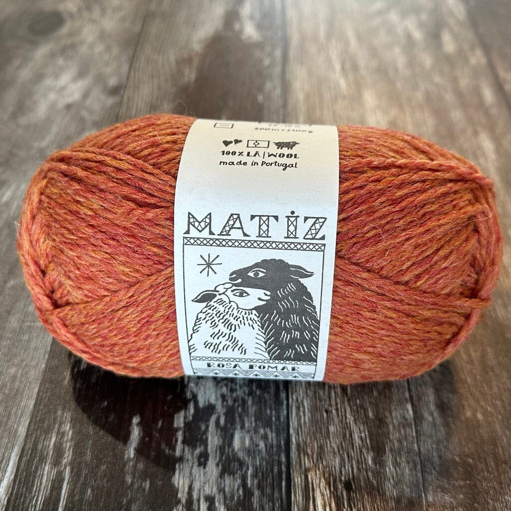 Ball of orange yarn with a 'Matiz' label on a wooden surface