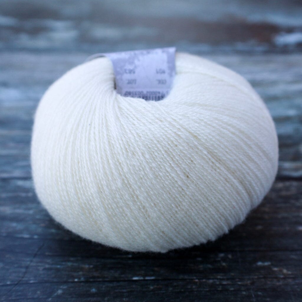 A ball of cream-colored yarn resting on a dark, rustic wooden surface. A small paper label is visible at the top of the yarn.