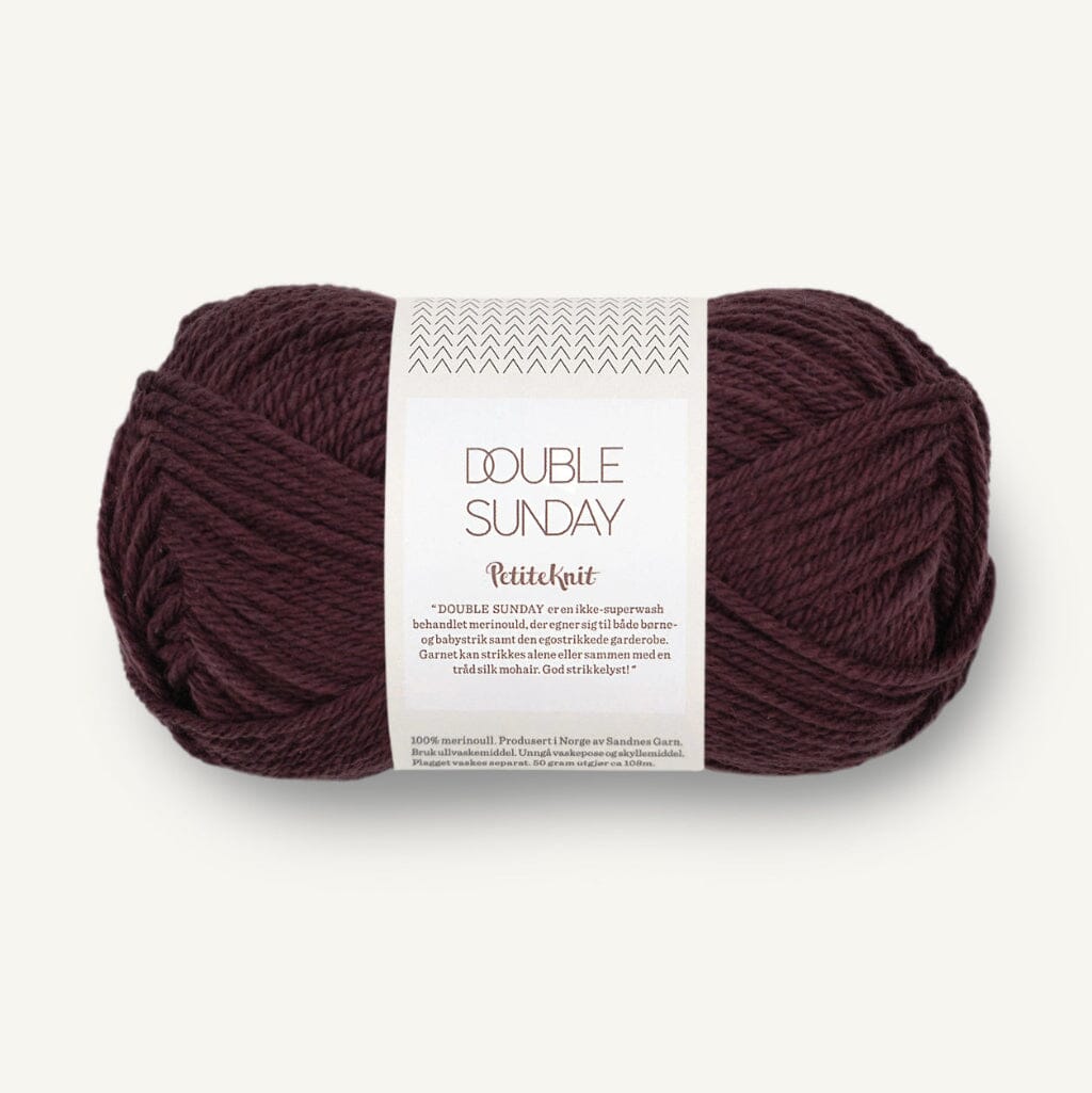 A skein of Double Sunday Petitclart yarn in a deep burgundy color, featuring a white paper label with black text, set against a clean off-white background.