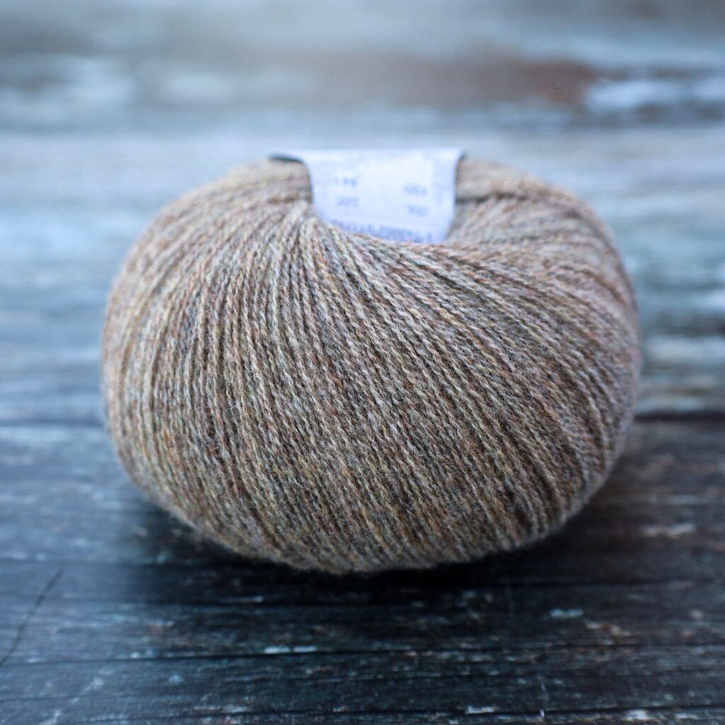 A single ball of heathered brown and beige yarn resting on a dark, rustic wooden surface. A small white paper label is visible at the top of the yarn.
