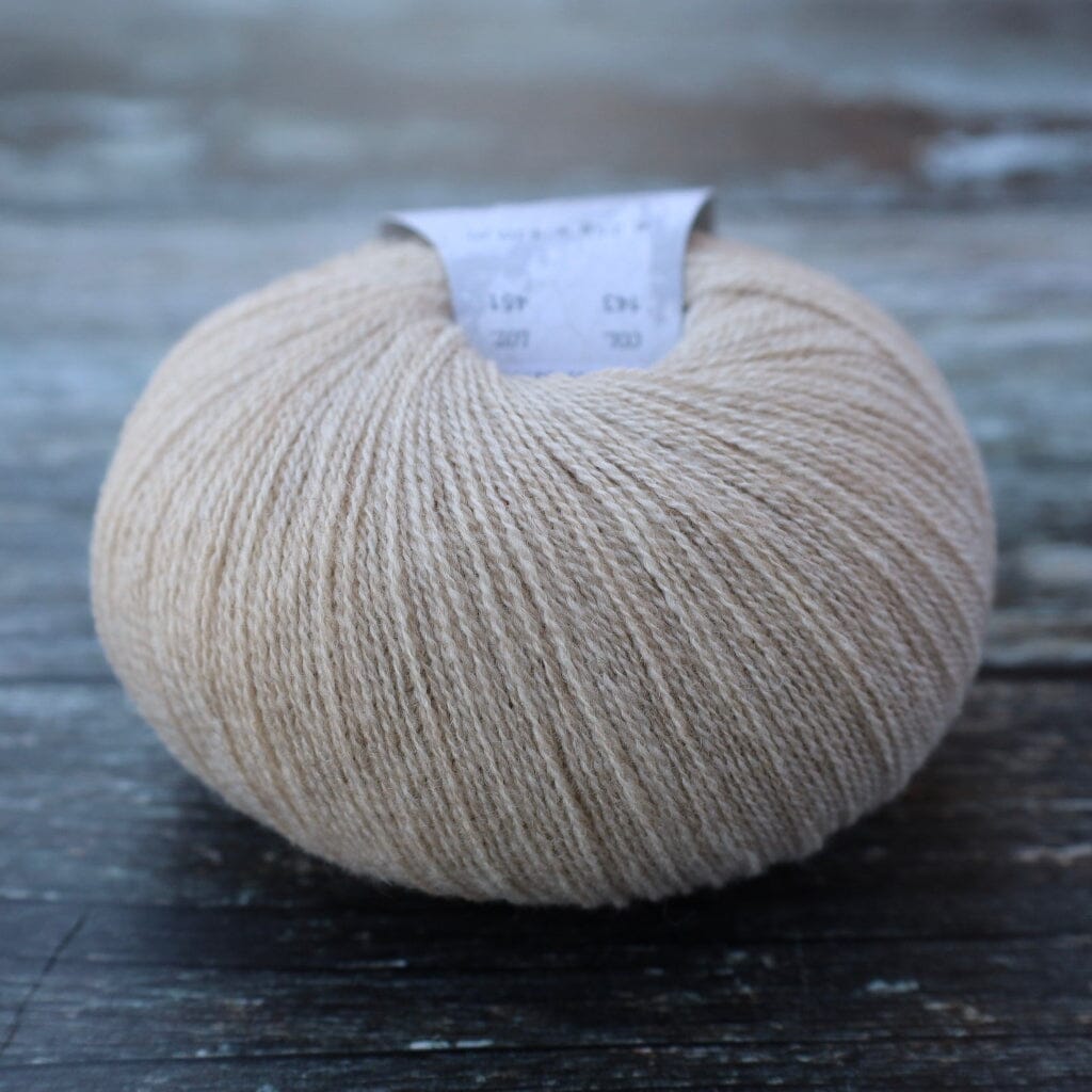 A ball of light beige yarn with a white paper label, resting on a dark, weathered wooden surface.