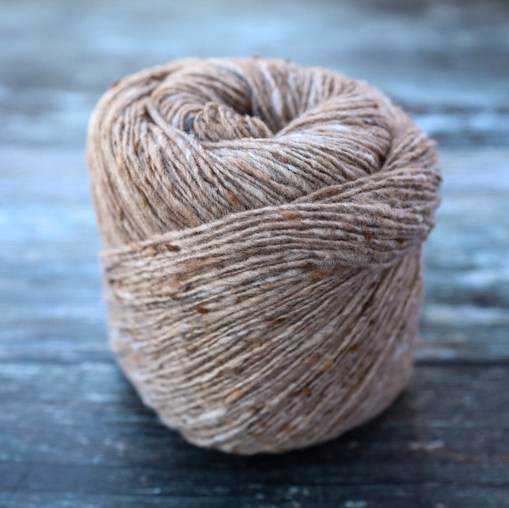 A ball of natural brown yarn with subtle beige and tan flecks, photographed on a rustic, weathered blue-gray wooden surface.