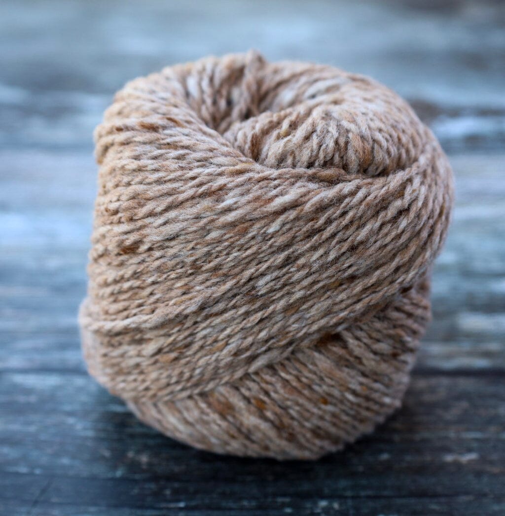 A ball of variegated brown and beige yarn wound on a spool, set against a rustic dark gray wooden background.