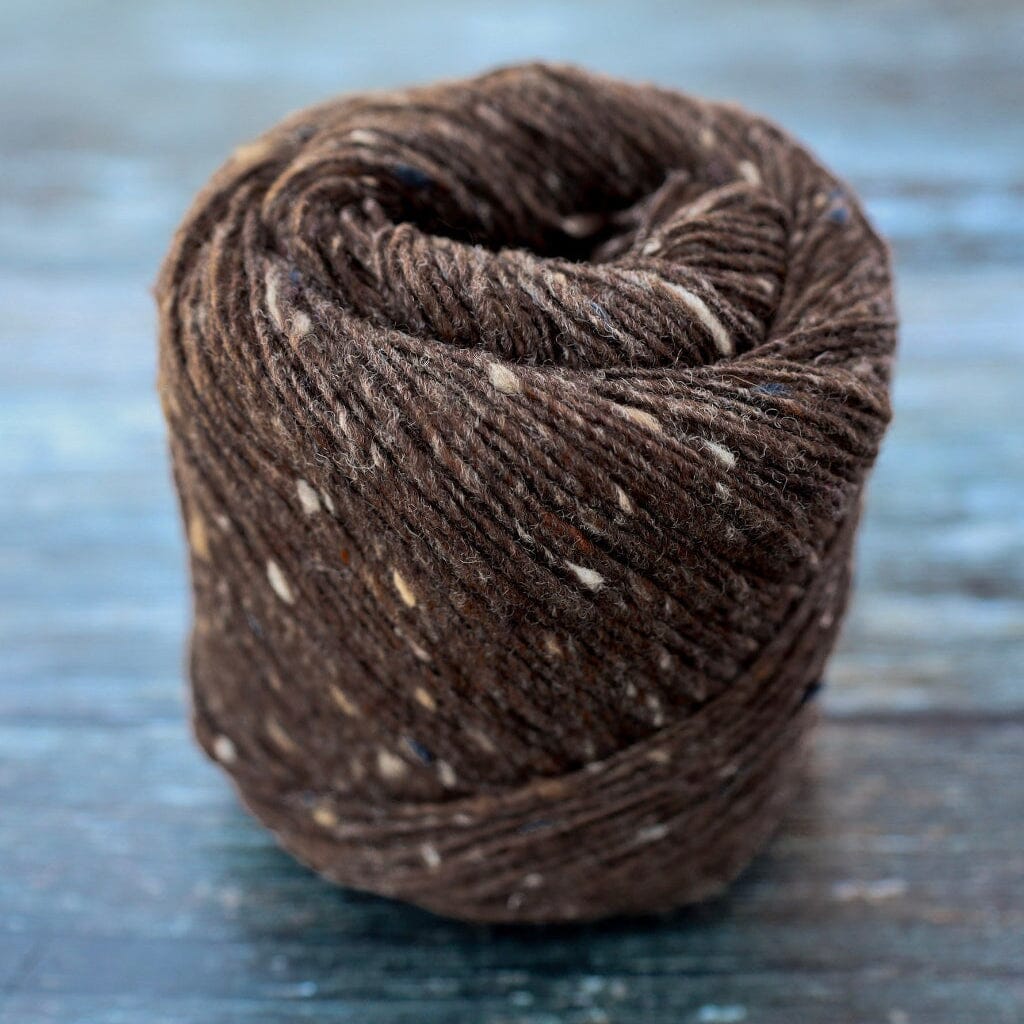 A close-up of a brown skein of yarn with white and beige flecks, wound into a coil on a rustic blue-gray wooden surface.
