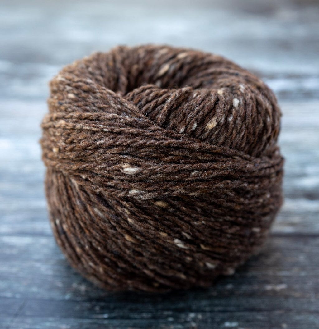 A ball of dark brown variegated yarn with lighter flecks, photographed on a rustic dark wooden surface.