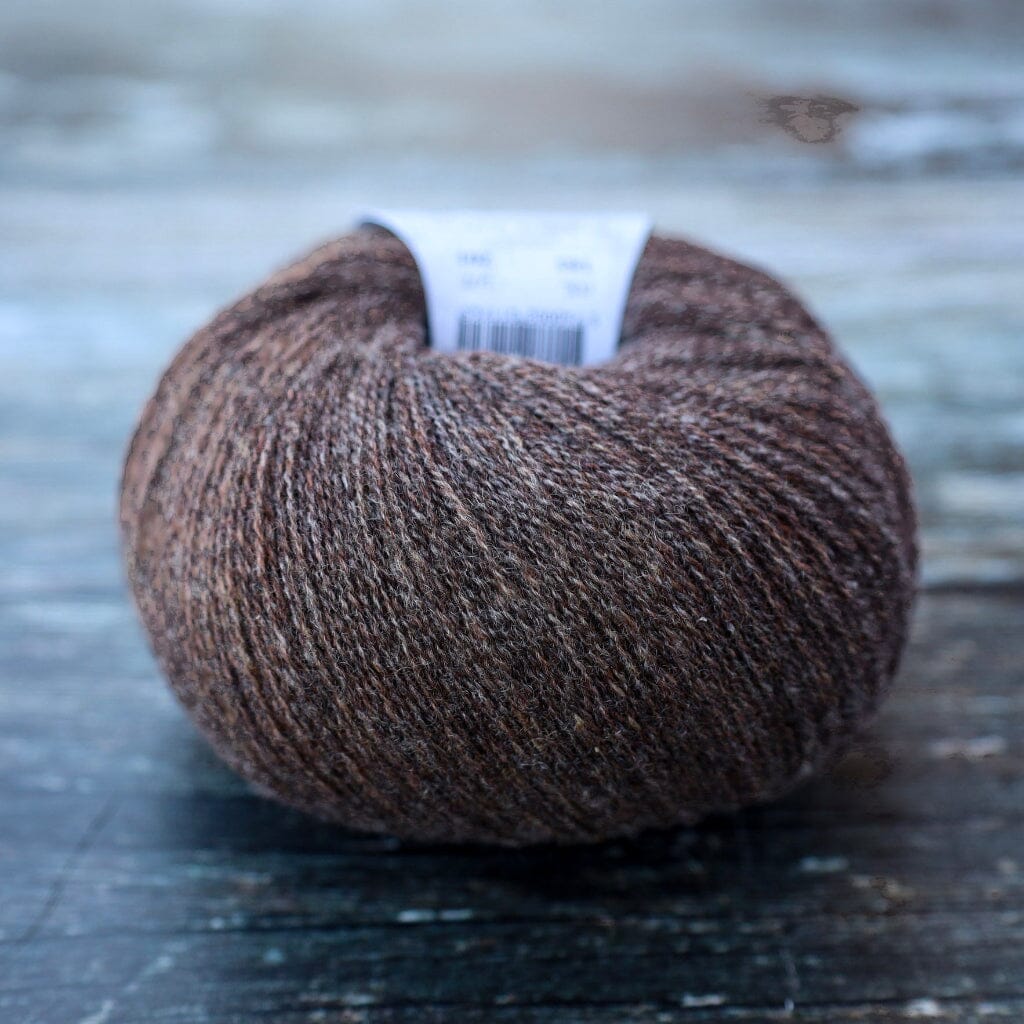 A single ball of brown heathered yarn with a white paper label, resting on a dark rustic wooden surface.