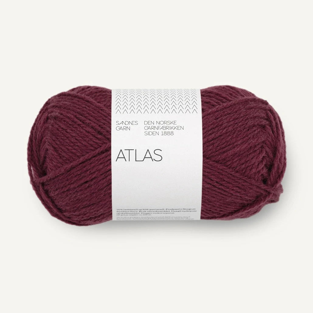 A skein of Atlas yarn in a deep burgundy color, wrapped with a white paper label that reads 'ATLAS' and 'SANDNES garn'.