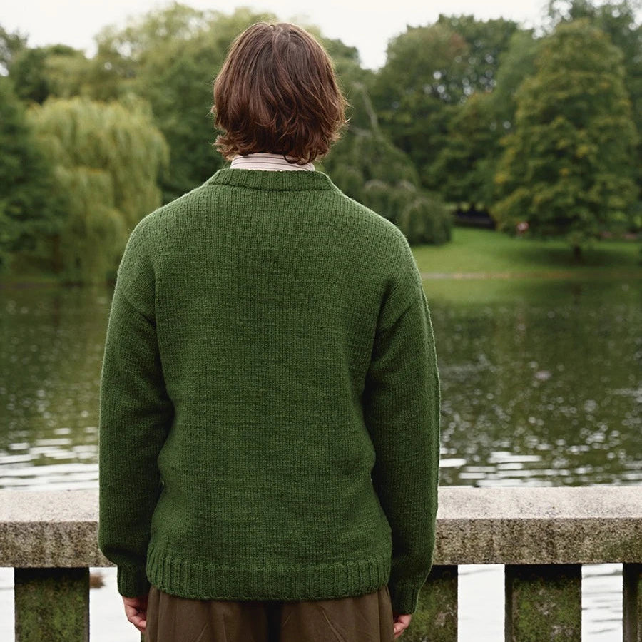 man wearing green knitted sweater standing with his bank to the camera