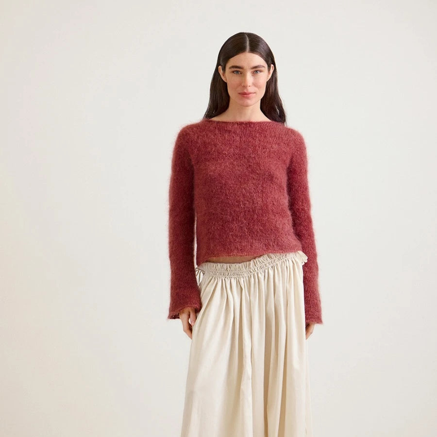 Woman wearing a maroon sweater and beige pants on a white background