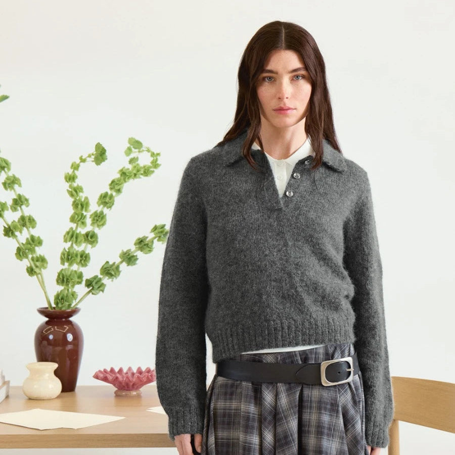 Woman wearing a grey sweater and plaid skirt in a room with a table and plants.
