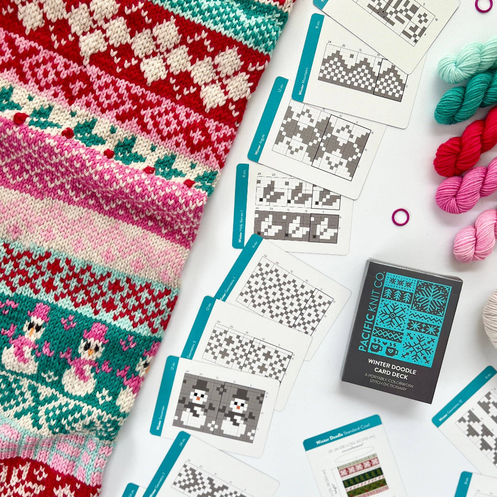 A hand holds a black box of Pacific Knit Co. Winter Doodle Card Deck, featuring a teal and black winter pattern graphic on the front.