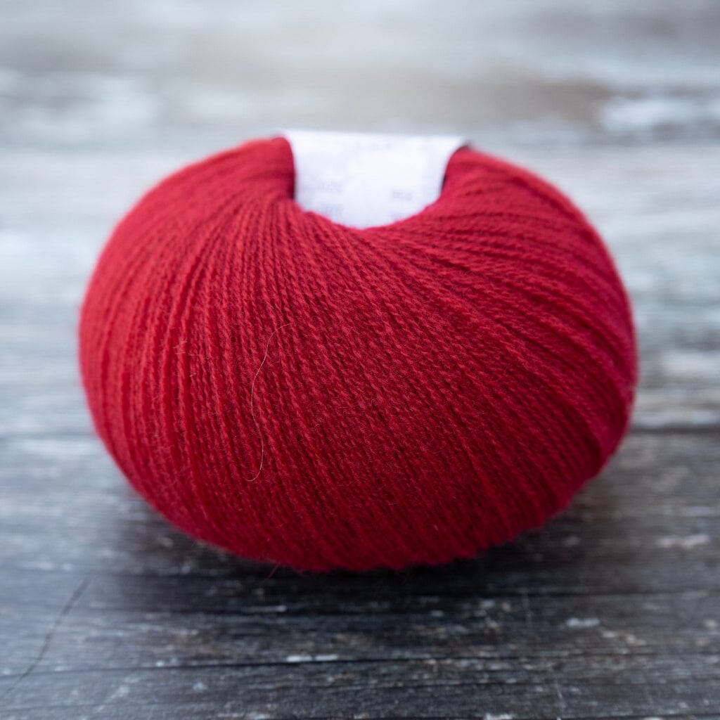 A ball of vibrant red yarn resting on a dark, weathered wooden surface.