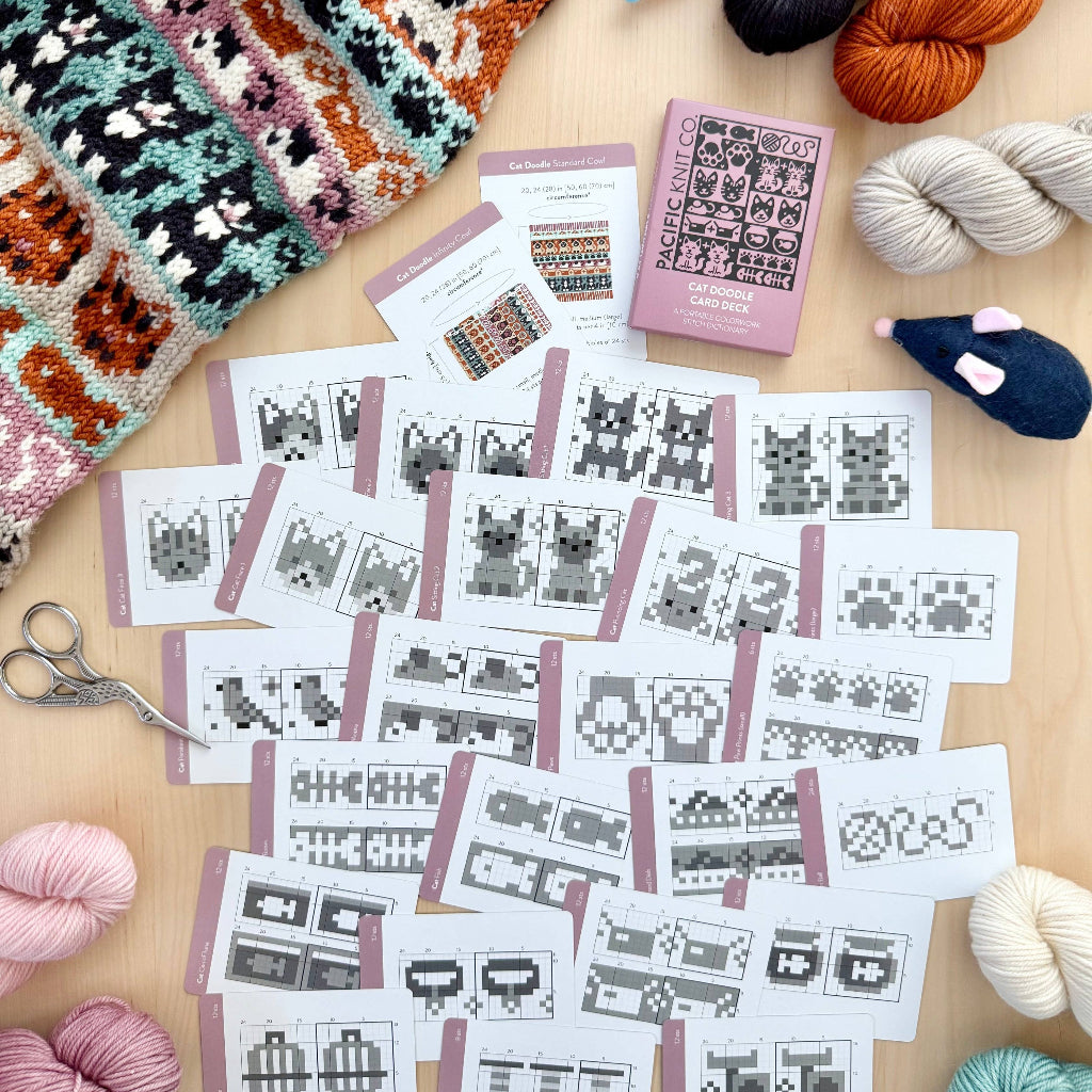 Knitting project with pattern cards, yarn, and knitting needles on a wooden surface