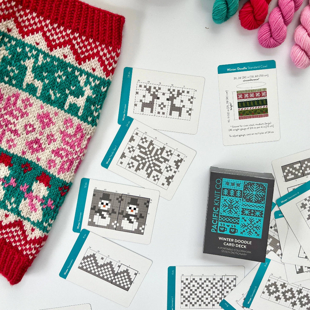 A flat-lay of a knitting pattern kit showing a completed festive red, green, and pink knitted sweater alongside various cards, yarn skeins