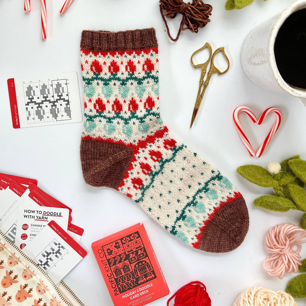 Knitted Christmas sock with yarn, scissors, and decorative items on a white surface