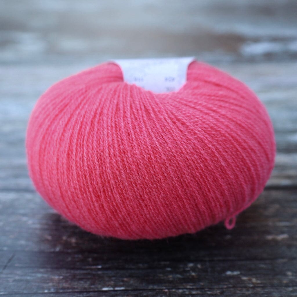 A ball of bright pink  yarn resting on a dark, weathered wooden surface.