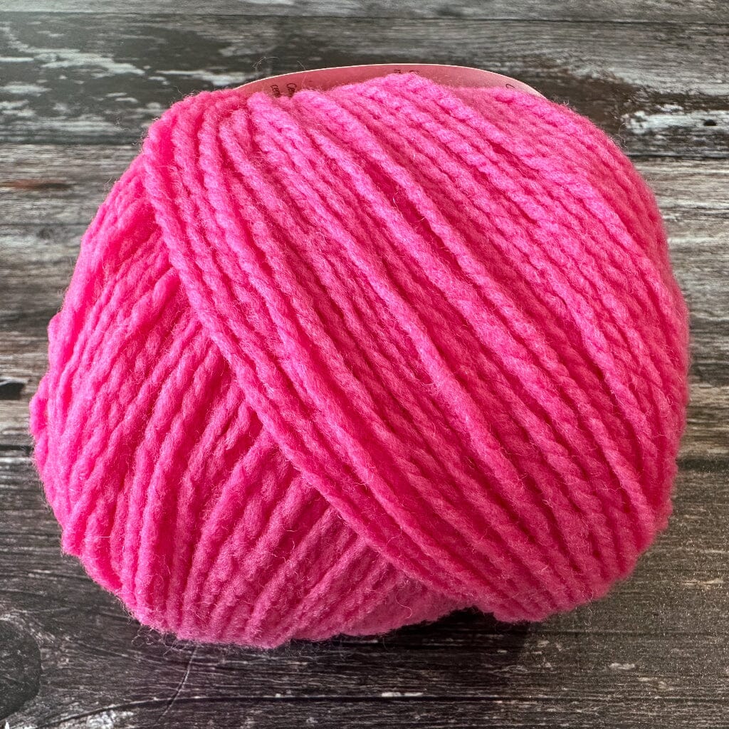 Ball of bright pink yarn on a wooden surface