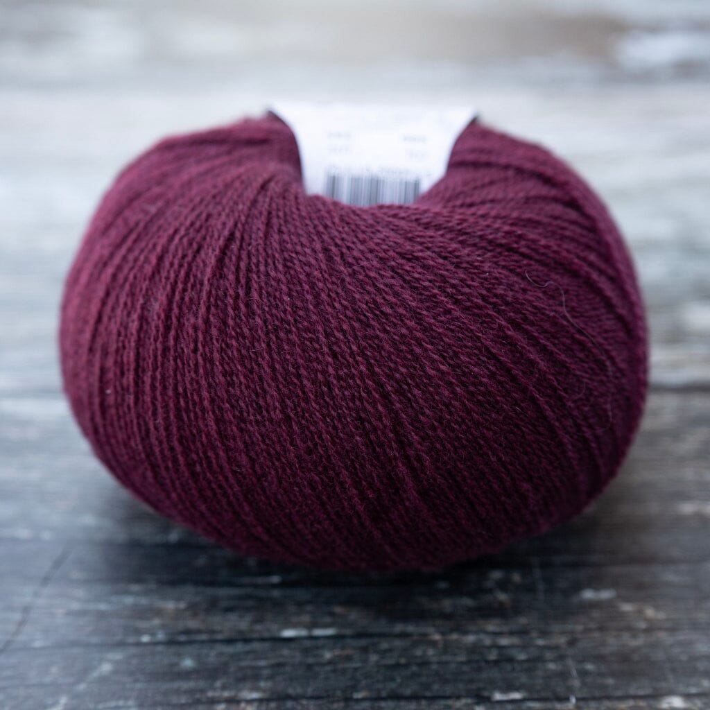 A single ball of dark burgundy yarn resting on a rustic, weathered dark wood surface. A white paper label is partially visible at the top of the ball.