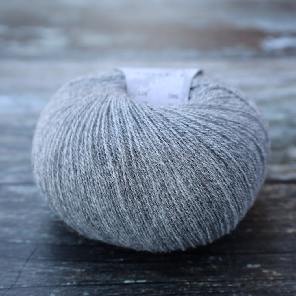 A ball of light gray heathered yarn resting on a rustic dark wooden surface, with a small white paper label visible at the top.