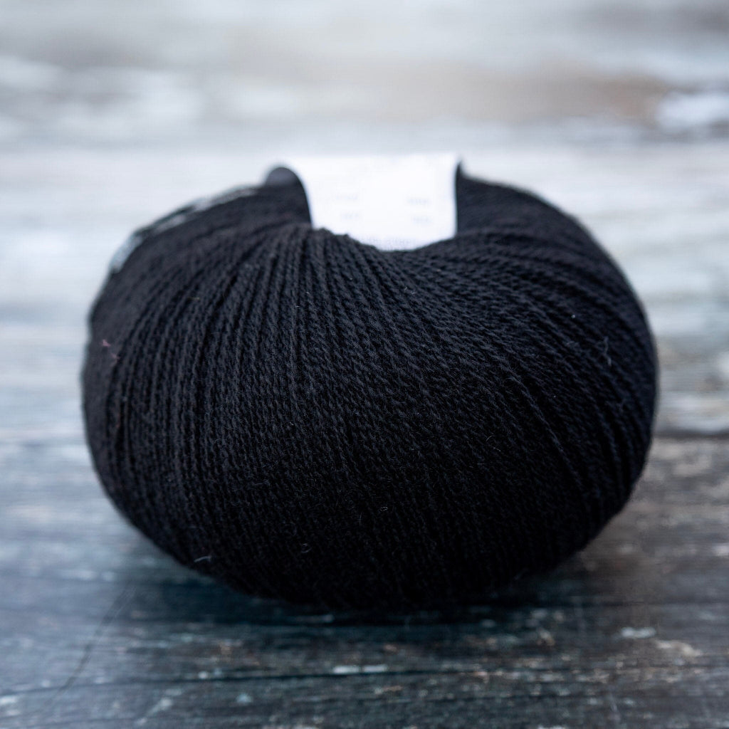 A single ball of black yarn resting on a rustic, weathered dark wooden surface.