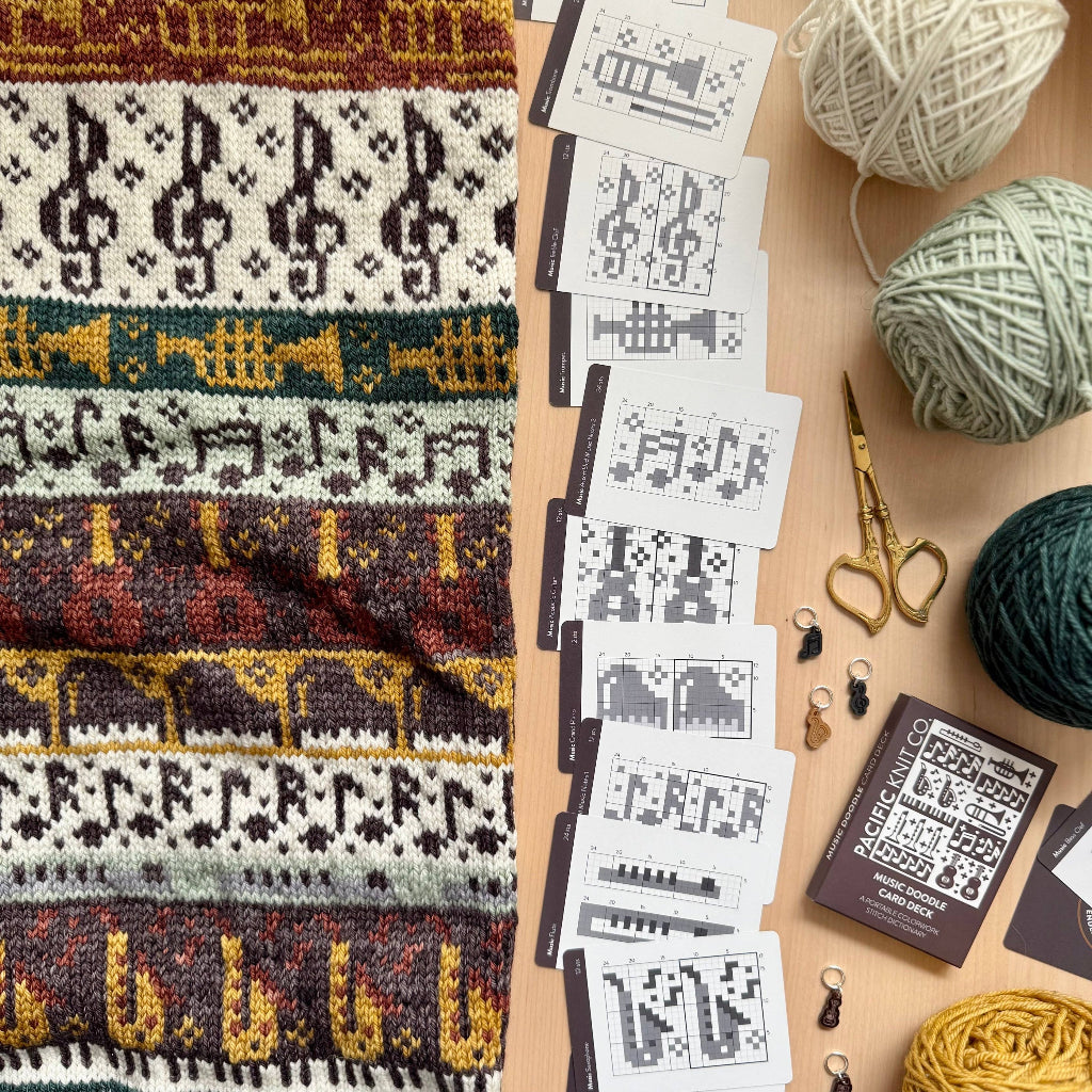 Knitted fabric with patterns, yarn balls, and pattern cards on a wooden surface