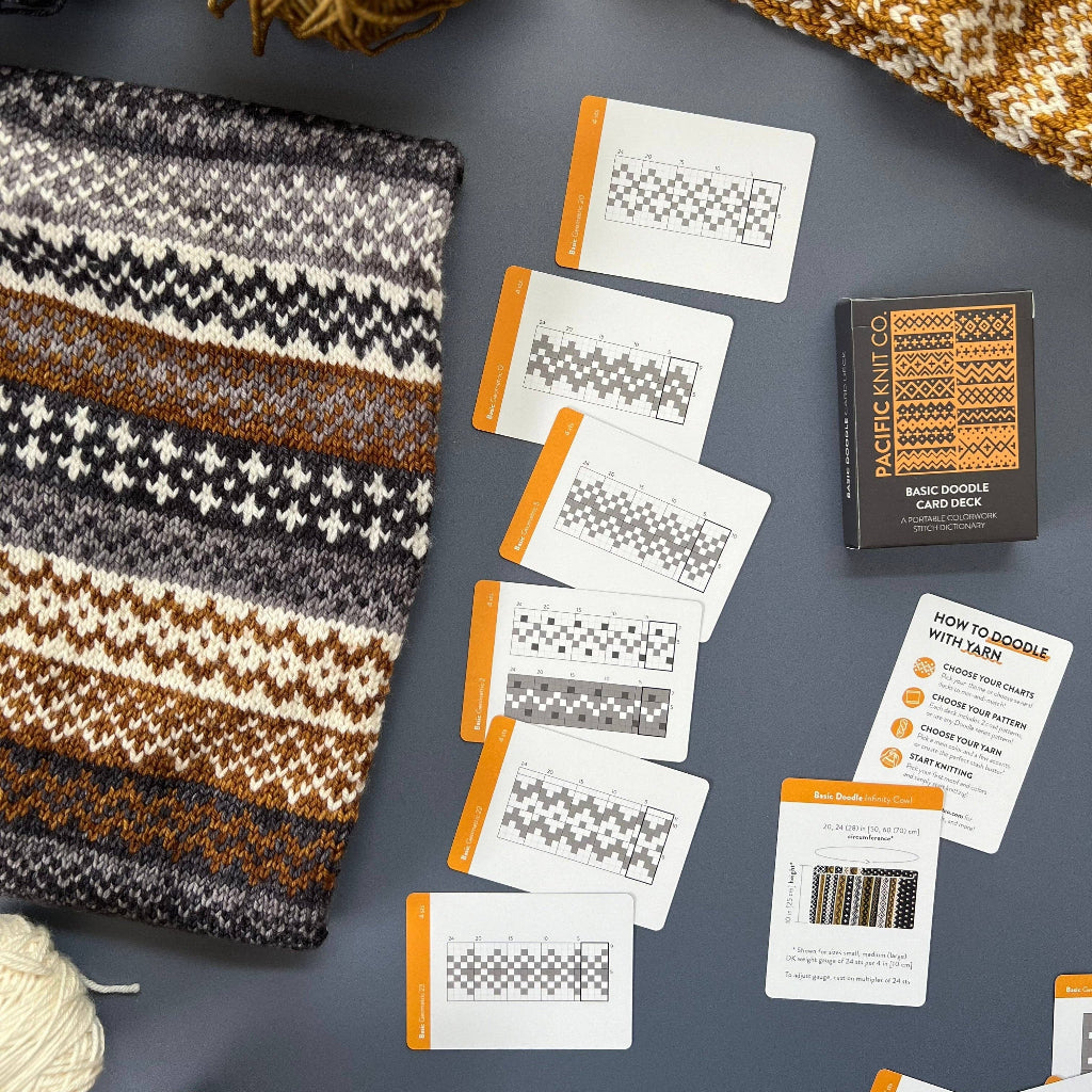 Knitted fabric, yarn balls, and pattern cards on a gray surface