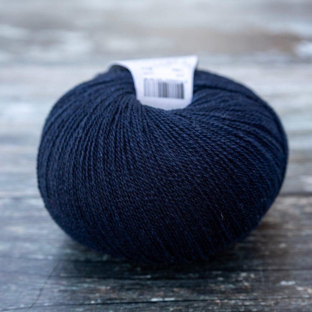 A single ball of dark navy blue yarn with a white paper label, resting on a rustic, weathered wooden surface.