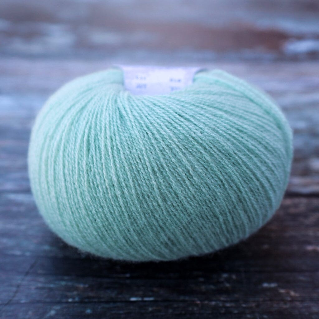 A ball of light mint green yarn resting on a dark, rustic wooden surface.