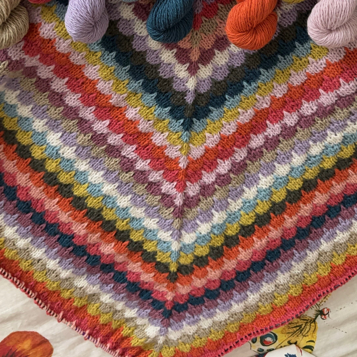Colorful knitted shawl with yarn balls in the background