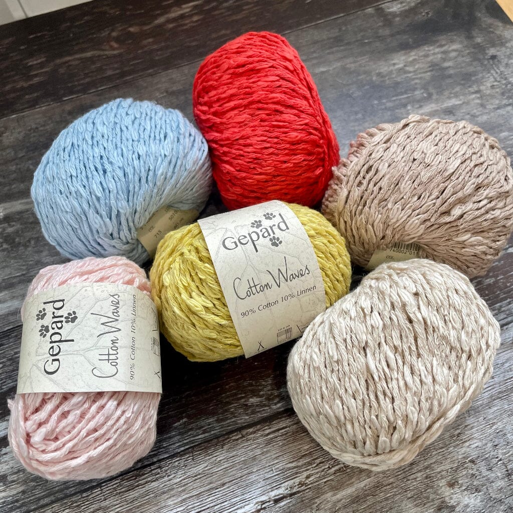 Five skeins of Gepard Cotton Waves yarn in various colors on a wooden surface.