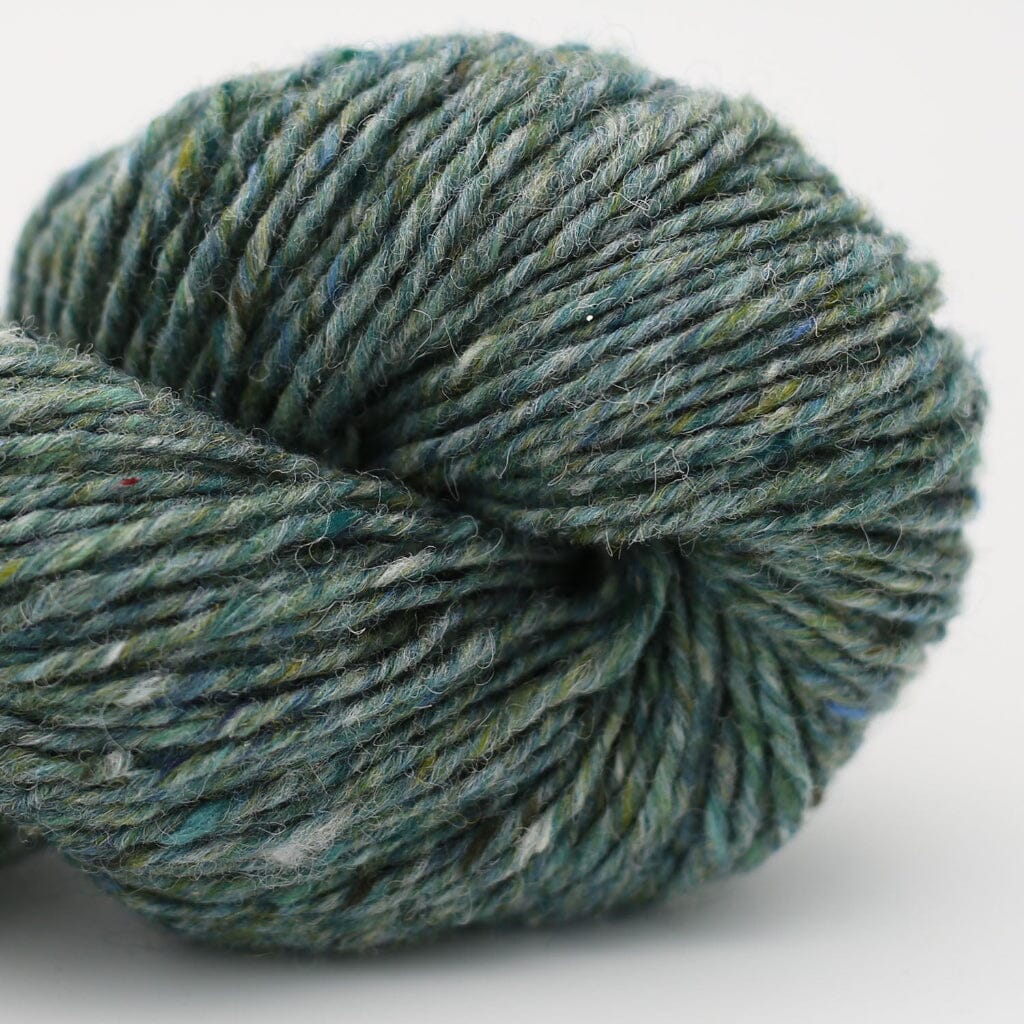 A close-up of a skein of variegated yarn in a muted teal-green color with subtle flecks of blue, white, and yellow, set against a plain light gray background.