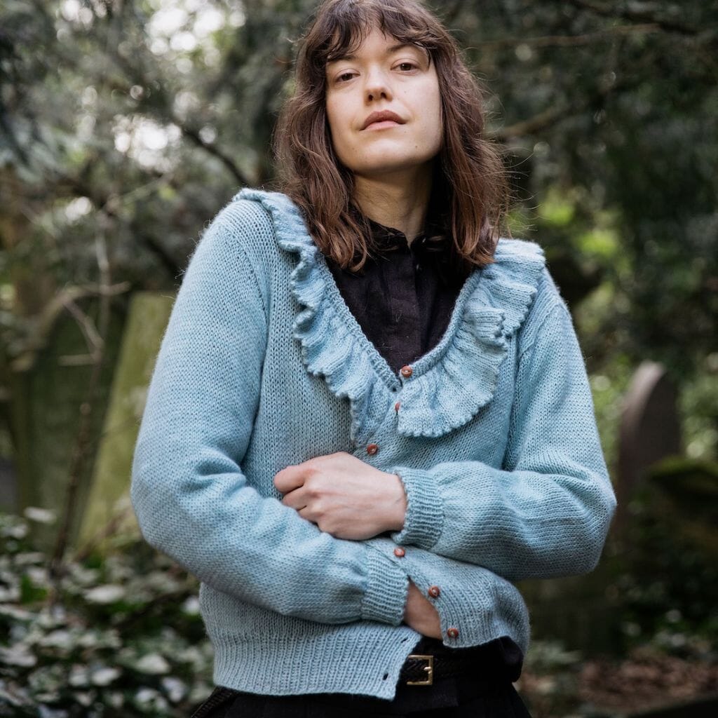 Woman wearing a light blue knitted cardigan with ruffled details outdoors.