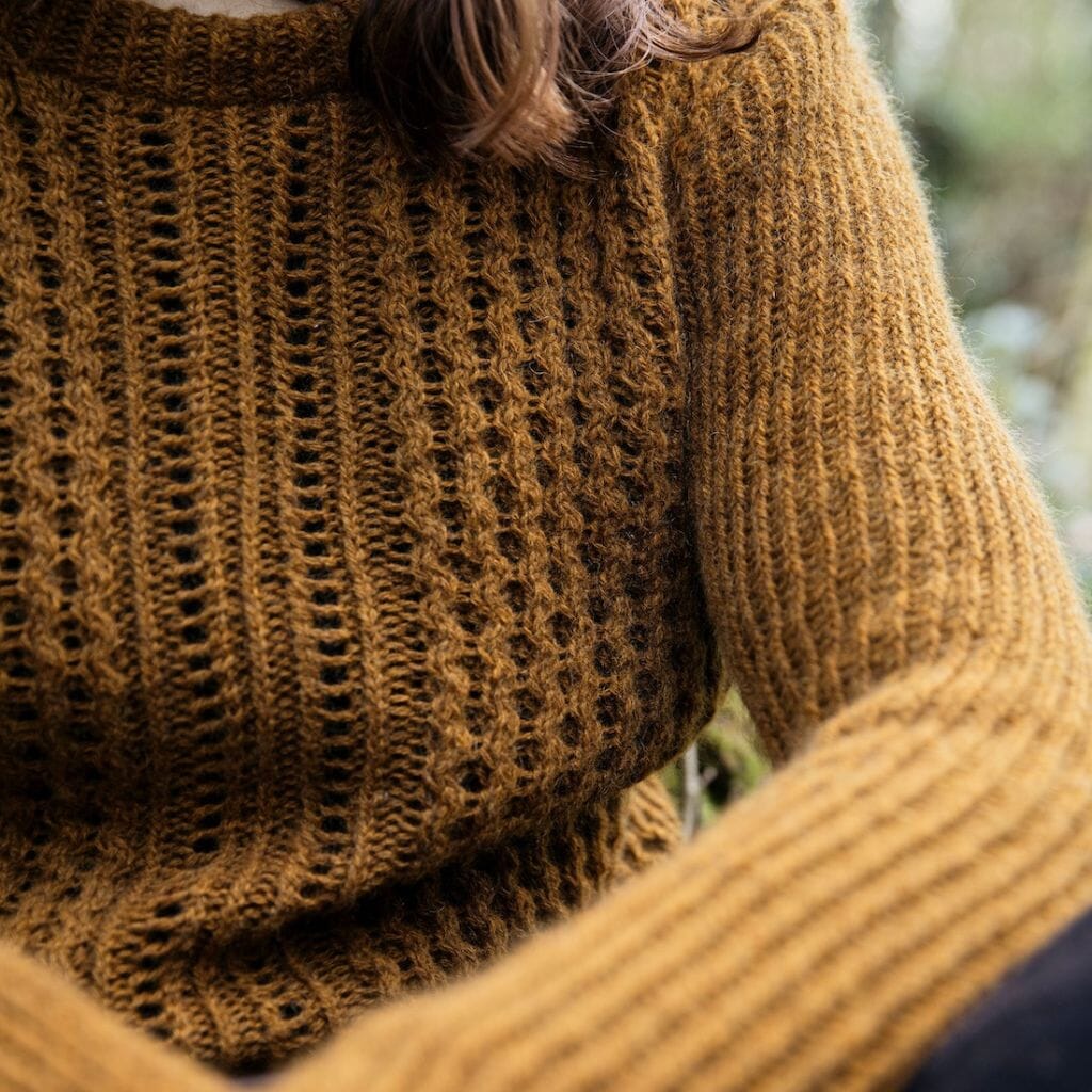 Close-up of a person wearing a brown cable knitted sweater with a blurred natural background