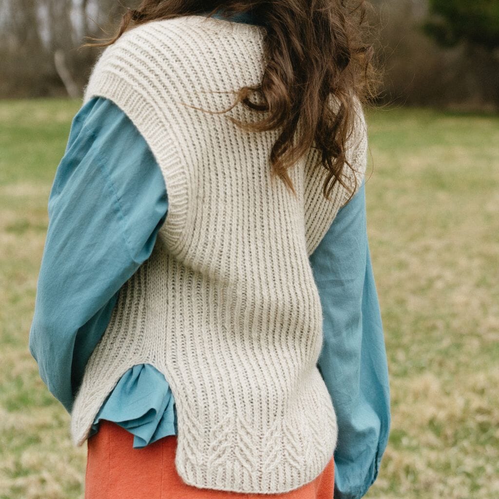 Person wearing a beige knitted vest over a blue shirt with a blurred natural background