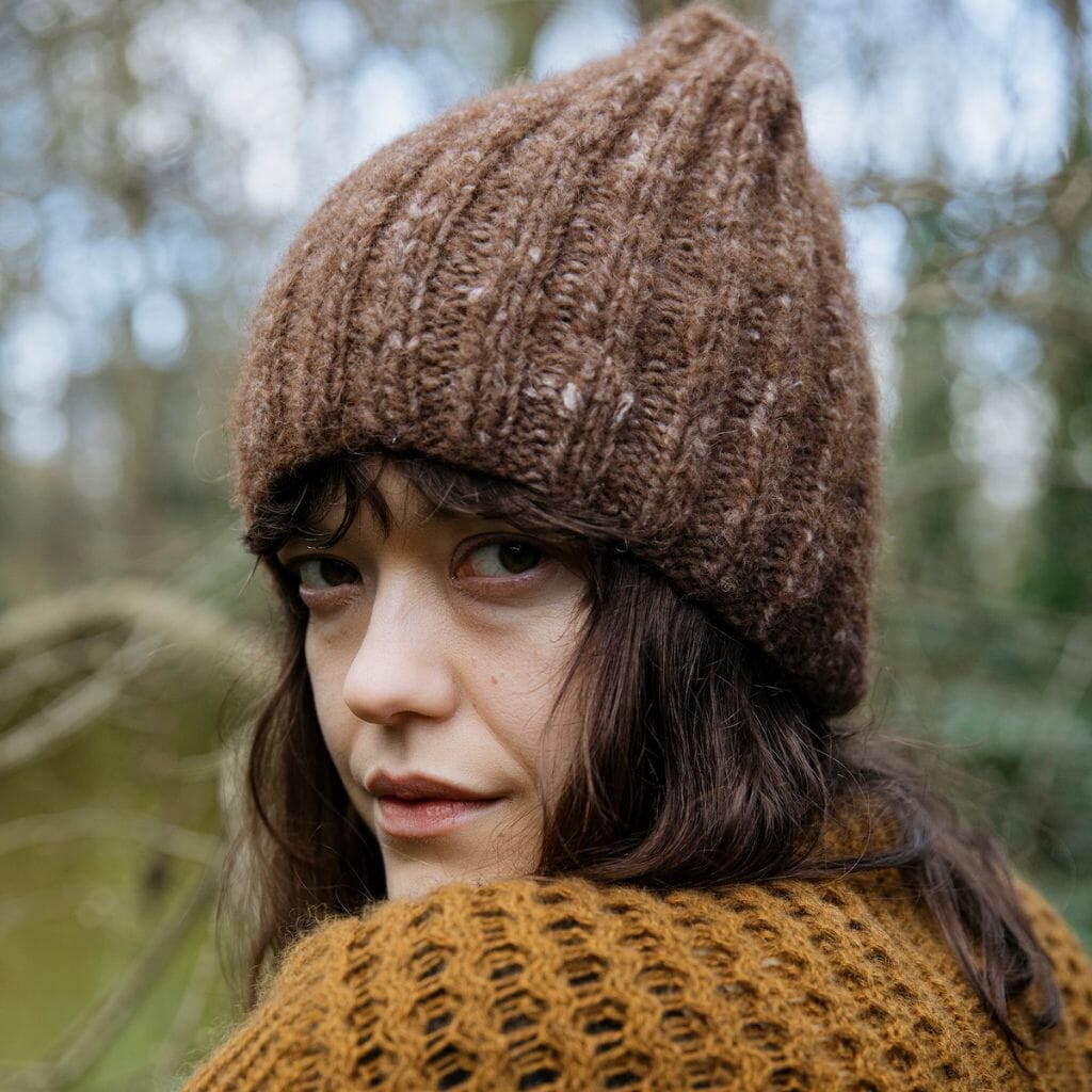Woman wearing a brown knit hat and sweater in a forest setting