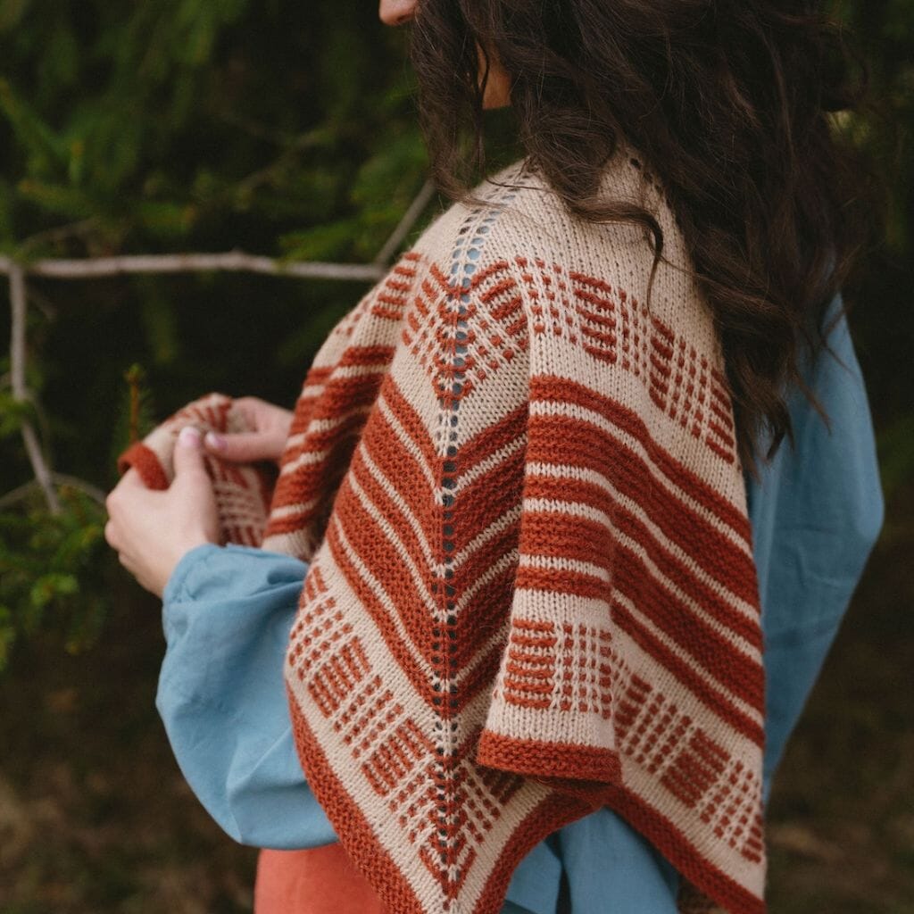Person wearing a patterned knitted shawl outdoors with greenery in the background