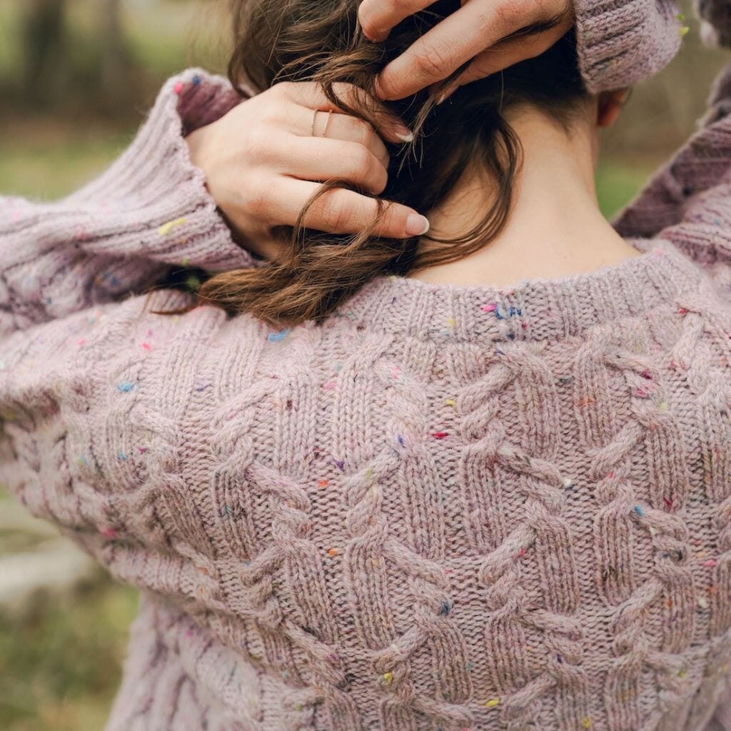 Person wearing a textured pink knitted sweater with blurred natural background