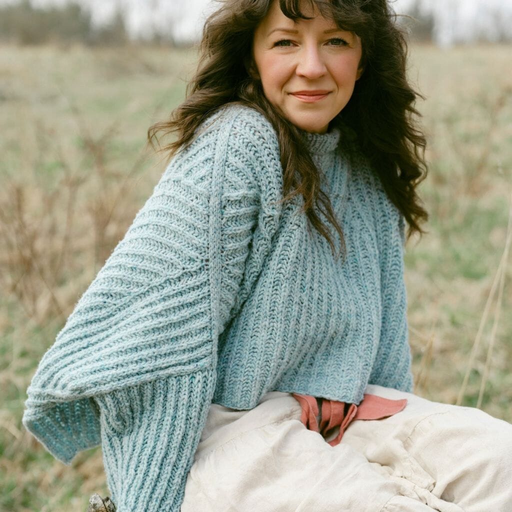 Woman wearing a teal knitted sweater sitting in a field