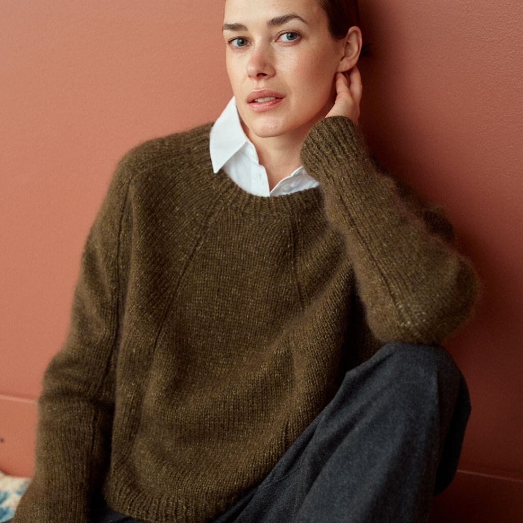 Woman wearing a brown sweater over a white shirt against a pink wall