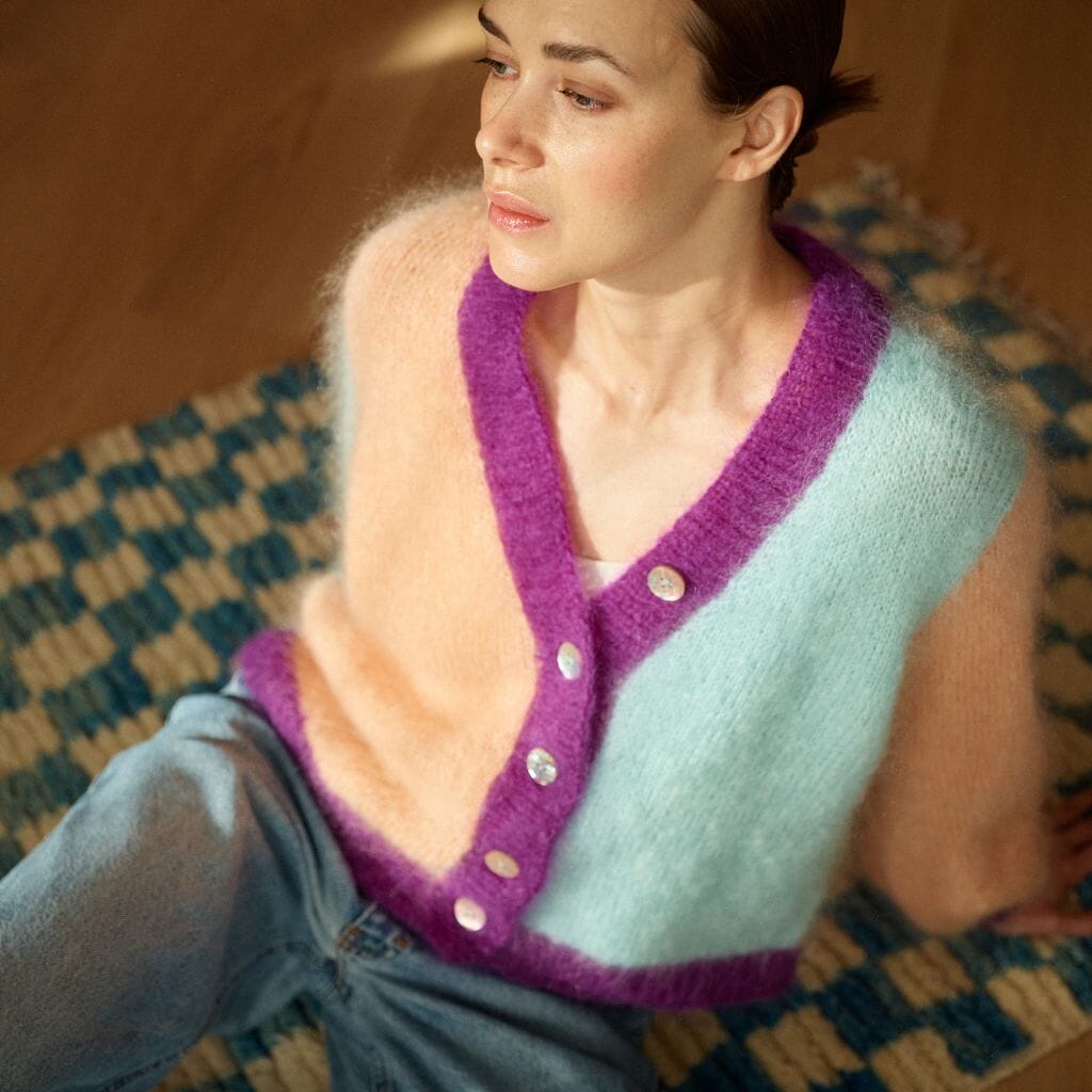 Woman wearing a light blue and purple cardigan sitting on a patterned rug.