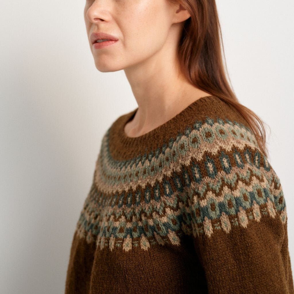Woman wearing a brown knitted sweater with a patterned yoke against a plain background