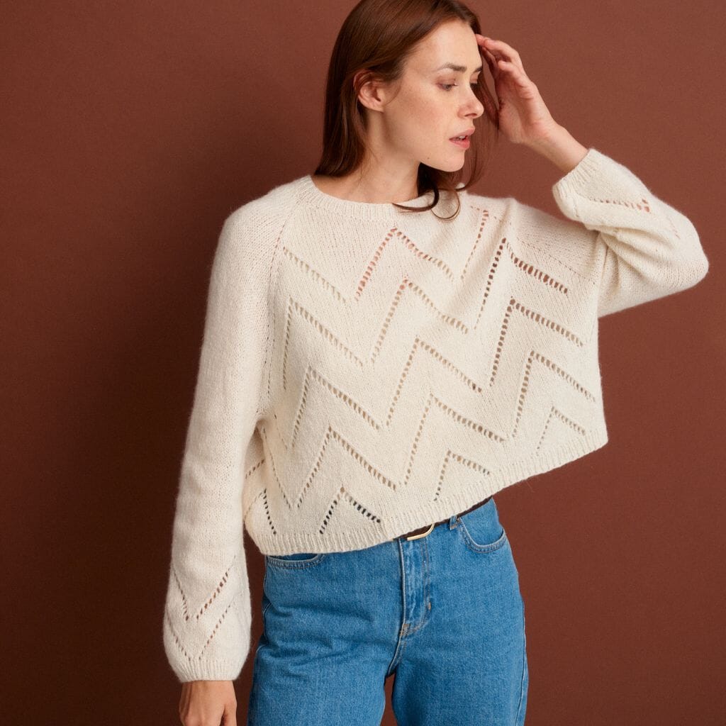 Woman wearing a cream sweater with a geometric pattern against a brown background
