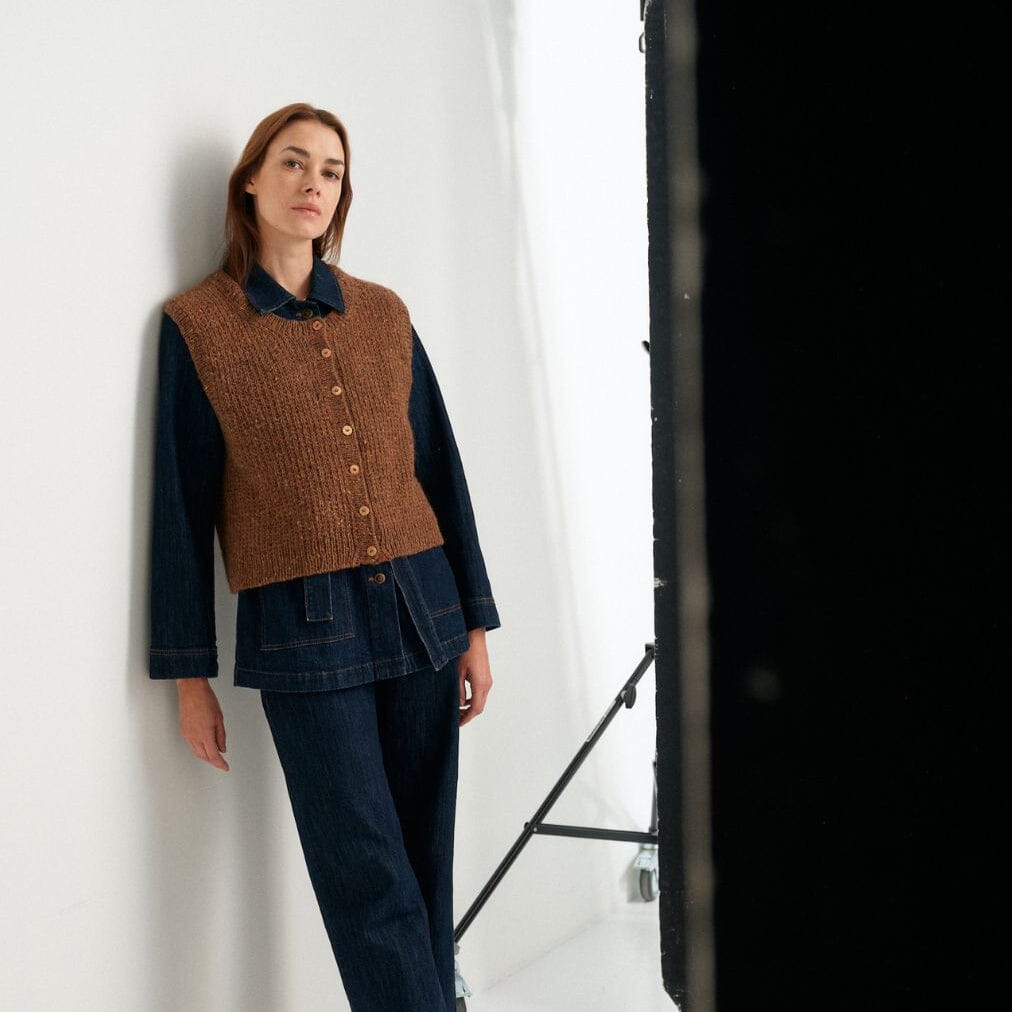 Woman wearing a brown knitted vest over a dark outfit against a white background