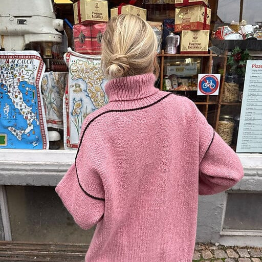 Person wearing a pink sweater standing in front of a store with various items on display.