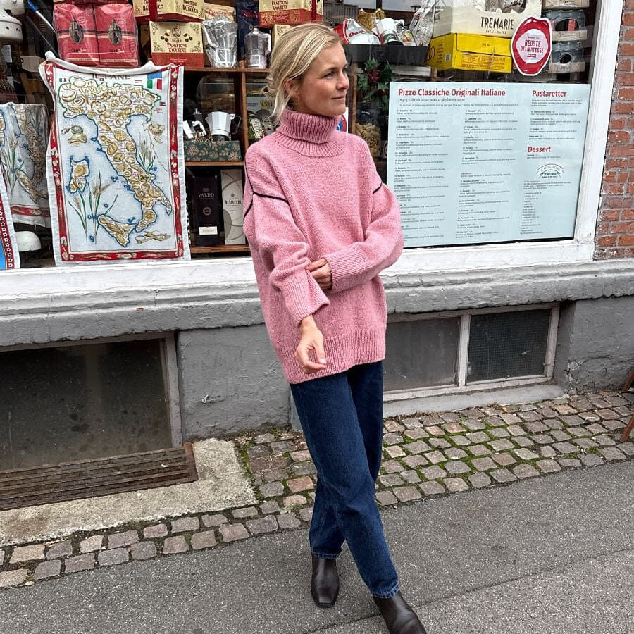 Woman in a pink sweater standing on a street in front of a store with various products.