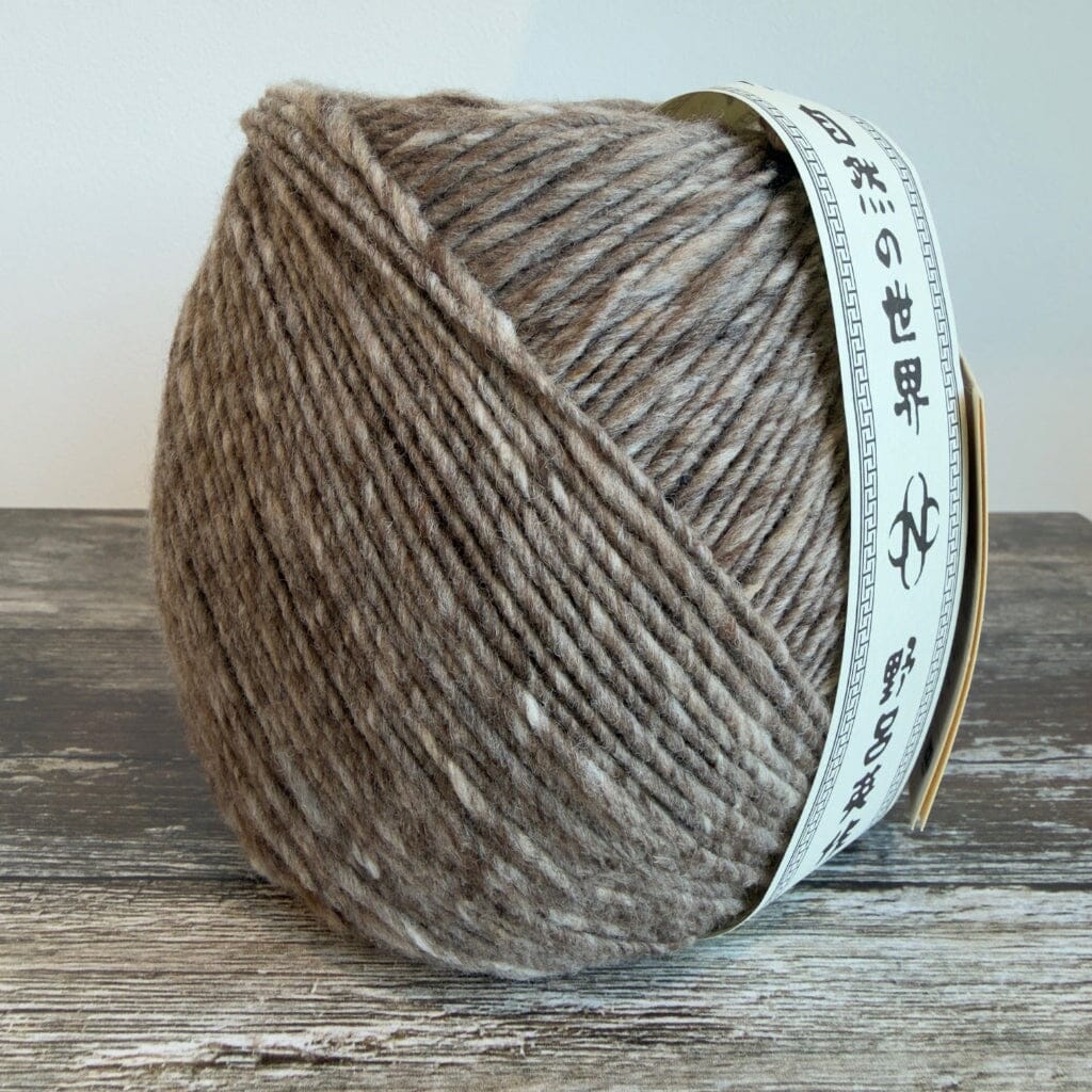 Three skeins of brown yarn with labels on a yellow surface