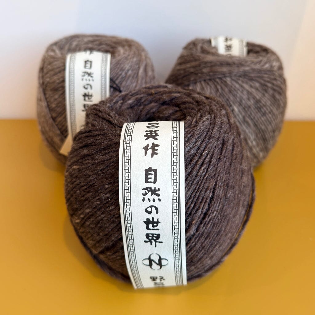Three skeins of brown yarn with labels on a yellow surface