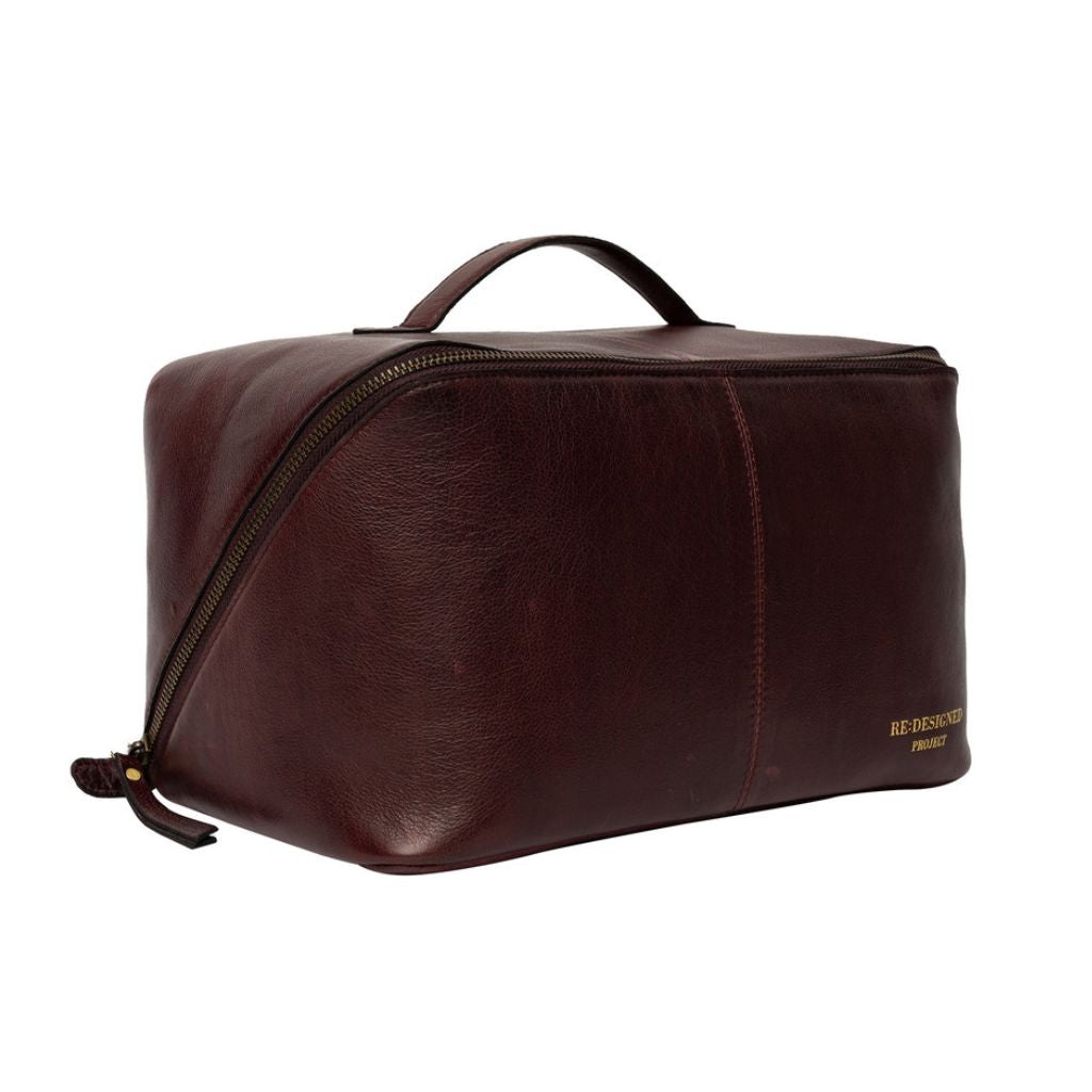 A dark brown leather knitting bag with a top handle, zippered closure, and gold branding on the bottom right corner, shown against a plain white background.