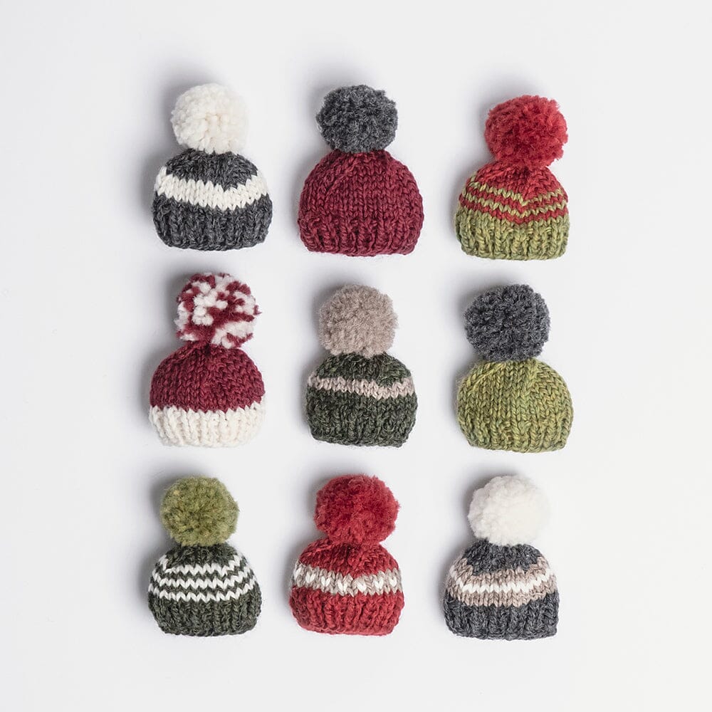 Set of small knitted hats with pom-poms in various colours on a light gray background
