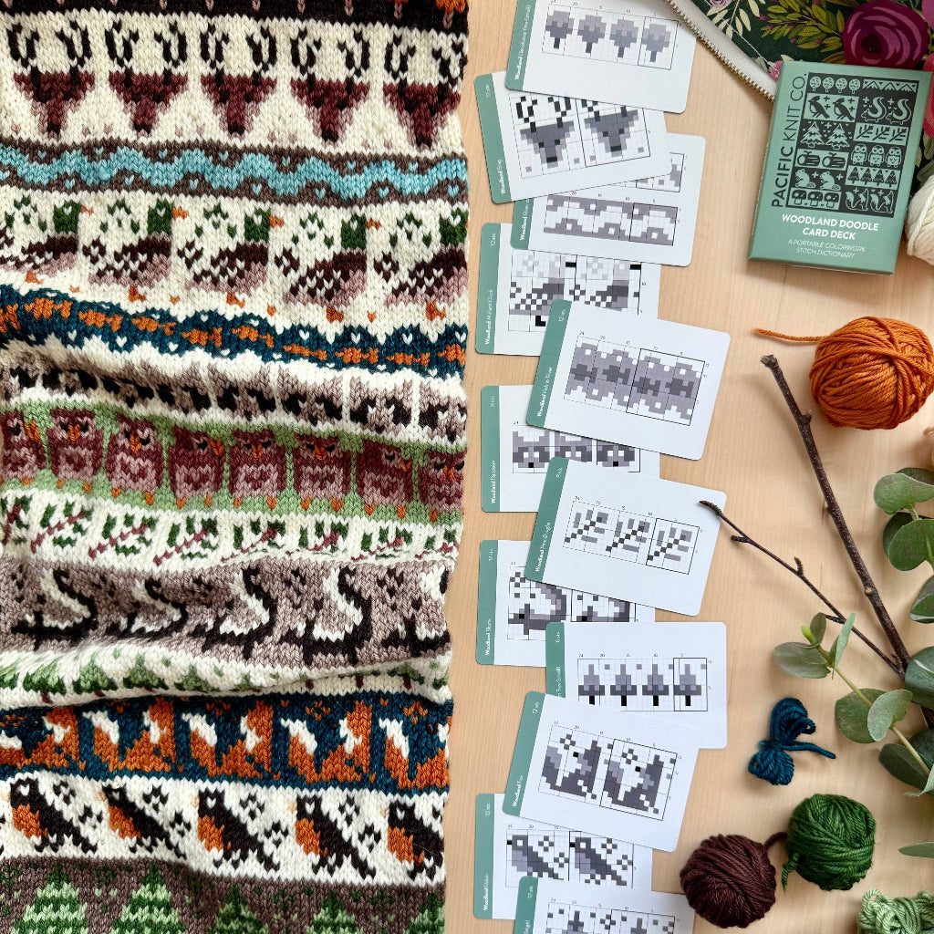 Knitted fabric with pattern, yarn balls, and knitting charts on a wooden surface